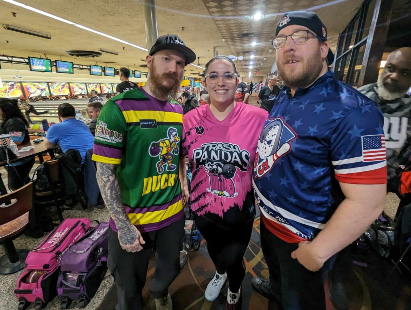 Three people participating in a league pose for a photo at a bowling alley.