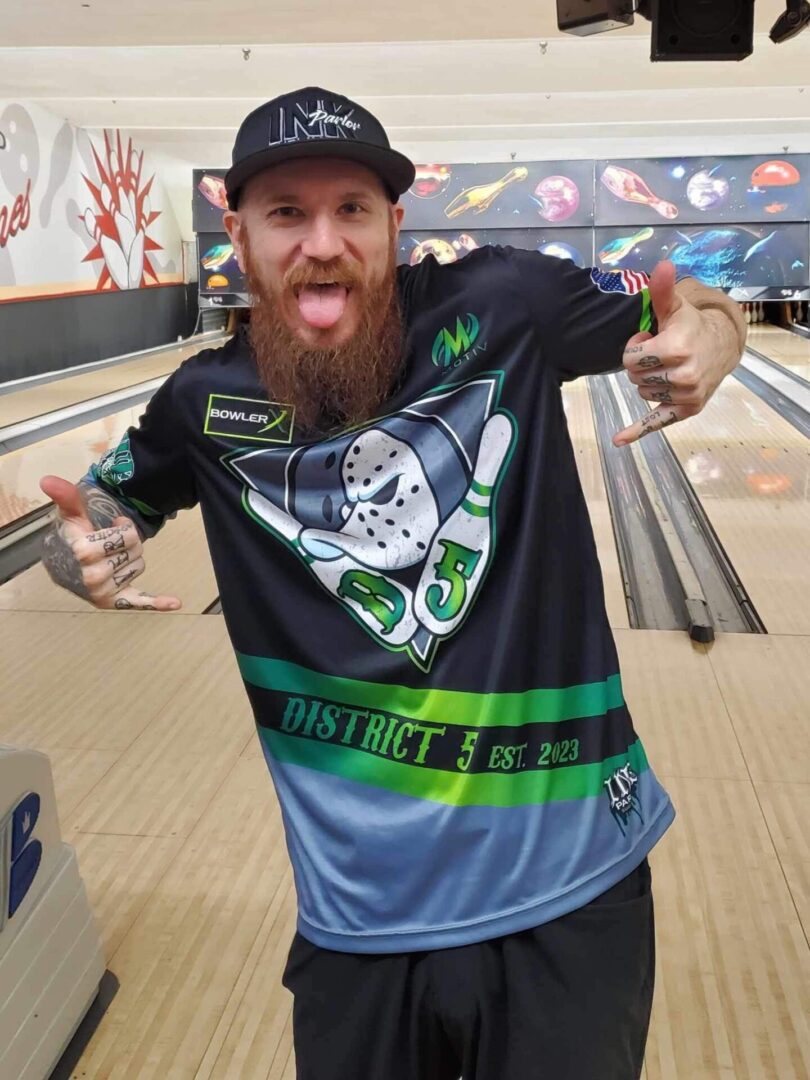 A man with a beard posing for a picture in a bowling alley.
