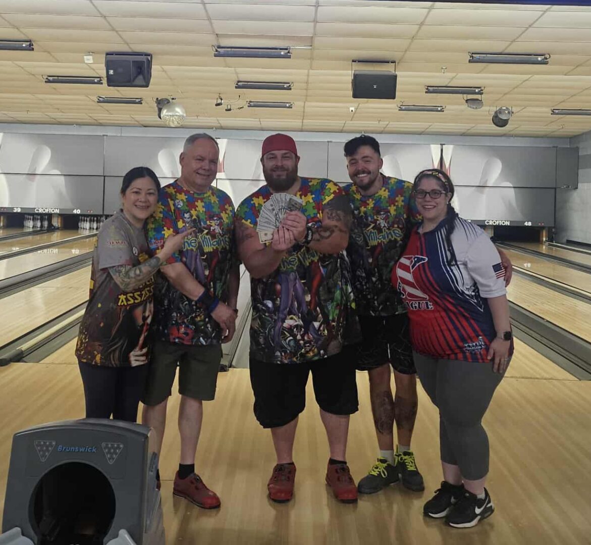 Five friends posing at a bowling alley, holding bowling balls.