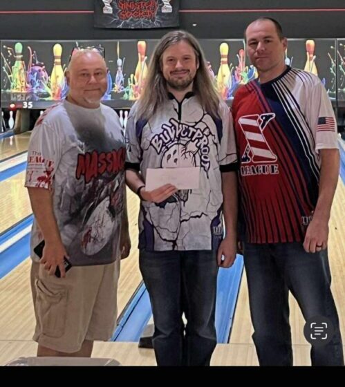 Three men posing together at a bowling alley.